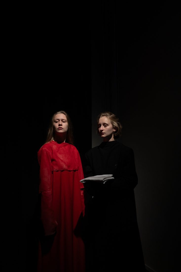Two performers in red and black on a dark stage